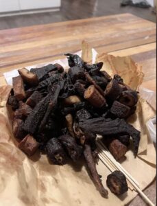 pile of overcooked or possibly burnt food items on a piece of paper, possibly resembling a type of grilled or fried snack on skewers. The dark color suggests they have been cooked for too long, giving them a charcoal-like appearance. The food items may be meat-based, potentially duck as referenced in earlier discussions about a similar incident, but it's difficult to identify precisely due to the level of cooking.