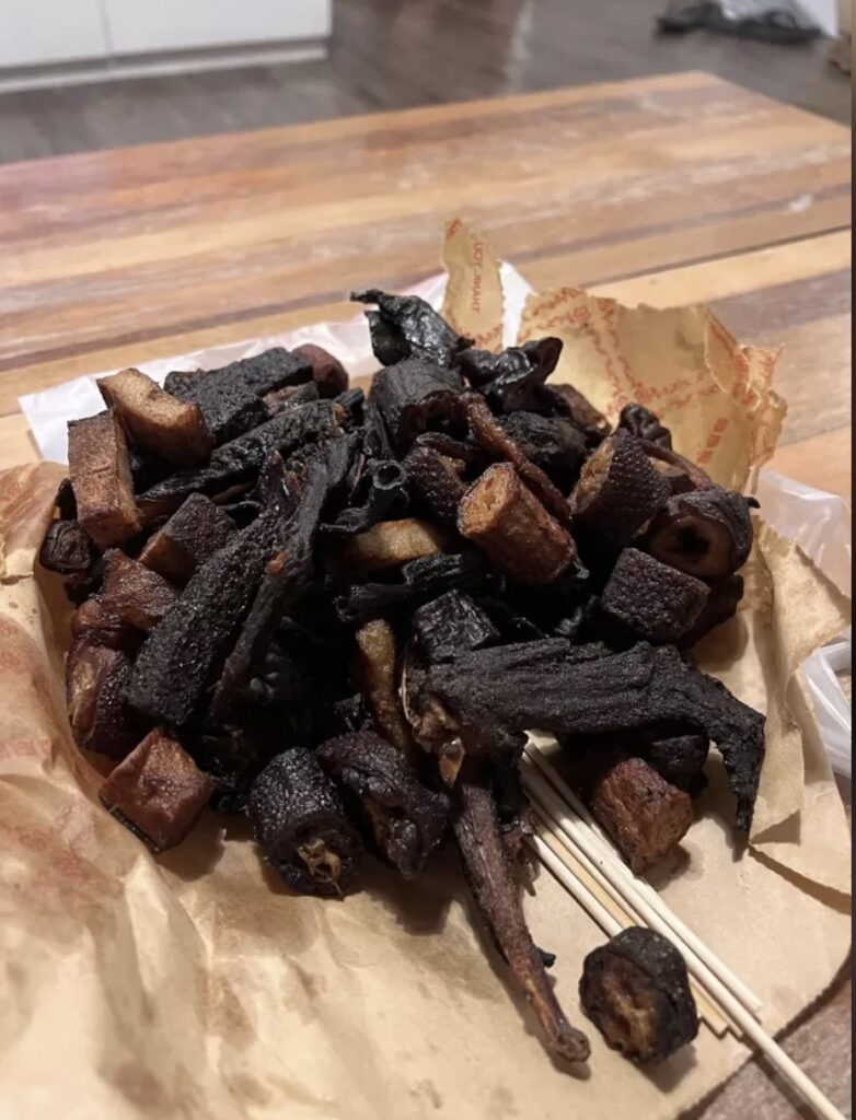 pile of overcooked or possibly burnt food items on a piece of paper, possibly resembling a type of grilled or fried snack on skewers. The dark color suggests they have been cooked for too long, giving them a charcoal-like appearance. The food items may be meat-based, potentially duck as referenced in earlier discussions about a similar incident, but it's difficult to identify precisely due to the level of cooking.